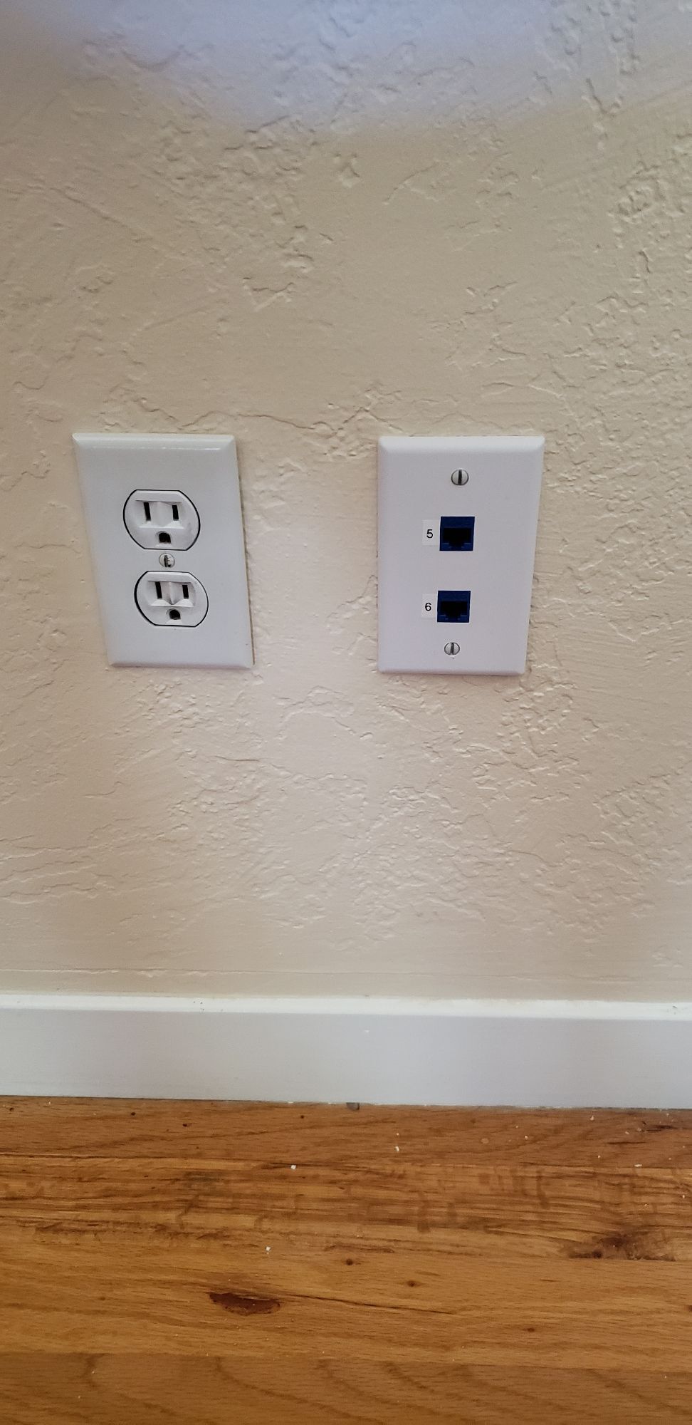 A couple of electrical outlets on a wall next to a wooden floor.