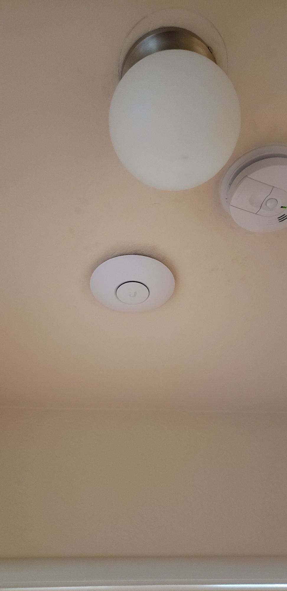 A ceiling with a light and a smoke detector on it.