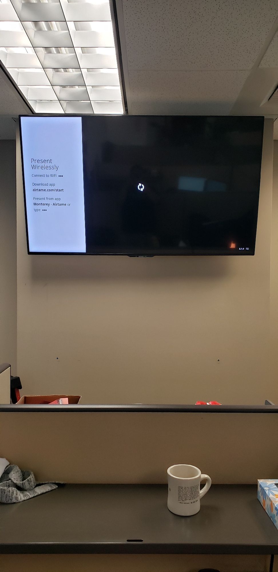 A coffee mug is sitting on a desk in front of a flat screen tv.