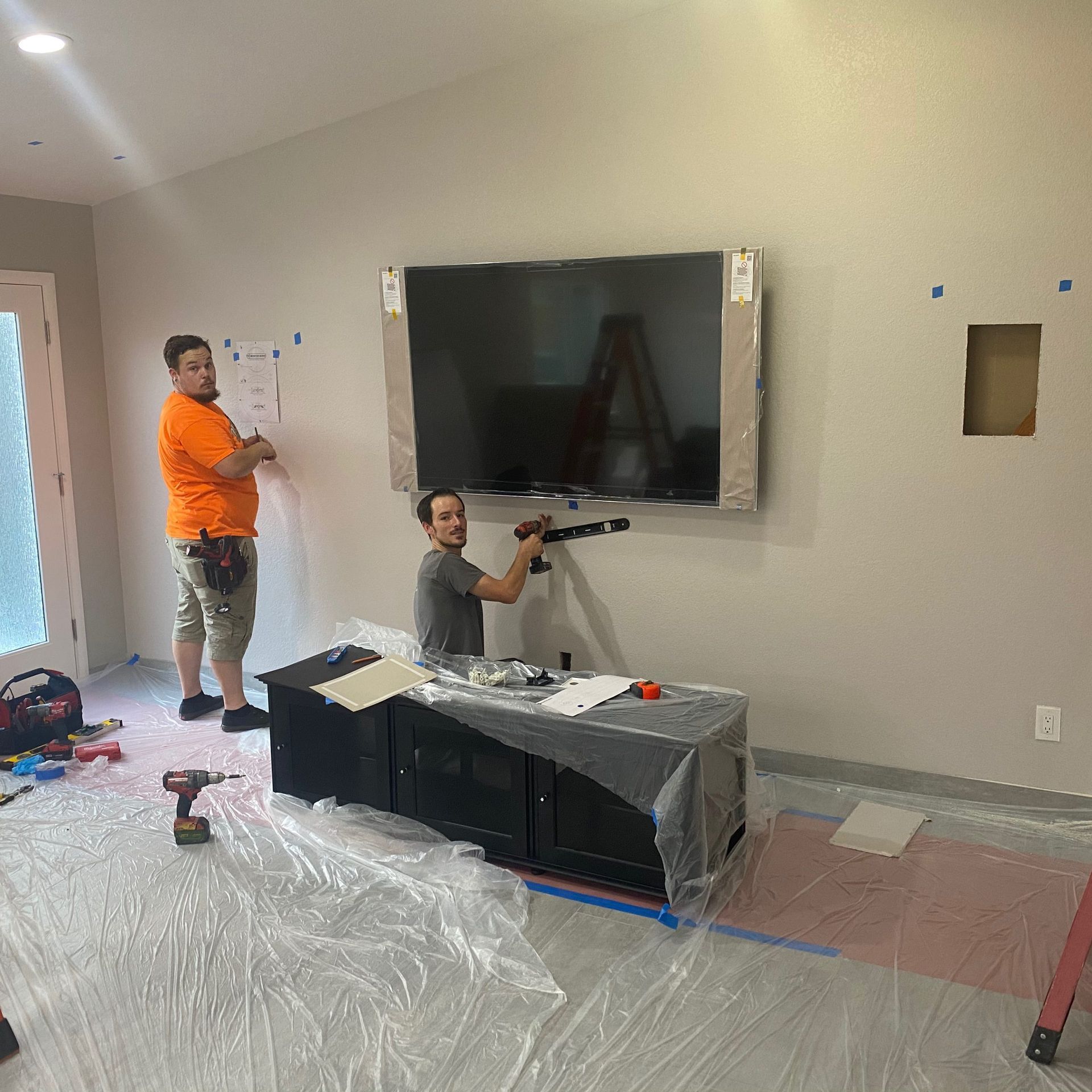 Two men are installing a flat screen tv on a wall.