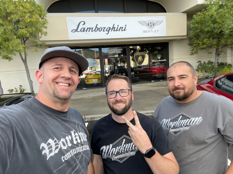 Three men are posing for a picture in front of a lamborghini store.