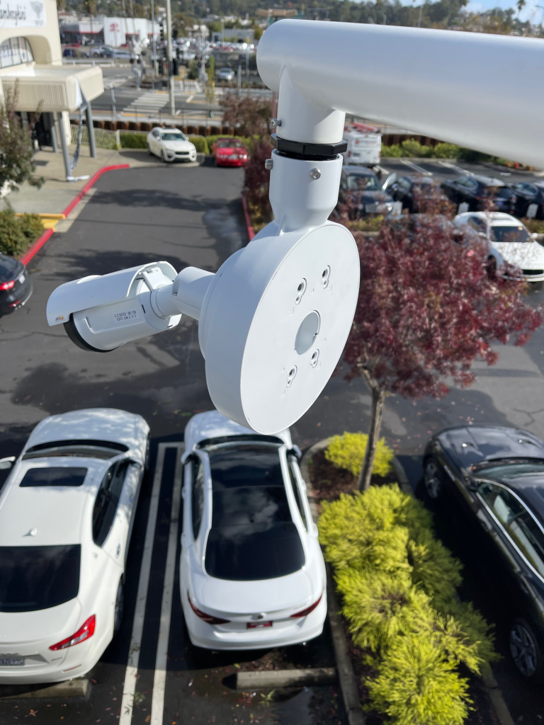 A white car is parked in a parking lot with a camera on top of it.