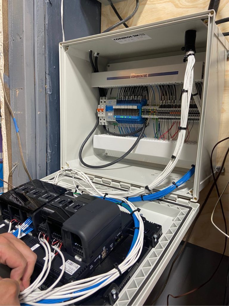 A person is working on a electrical box with a lot of wires coming out of it.