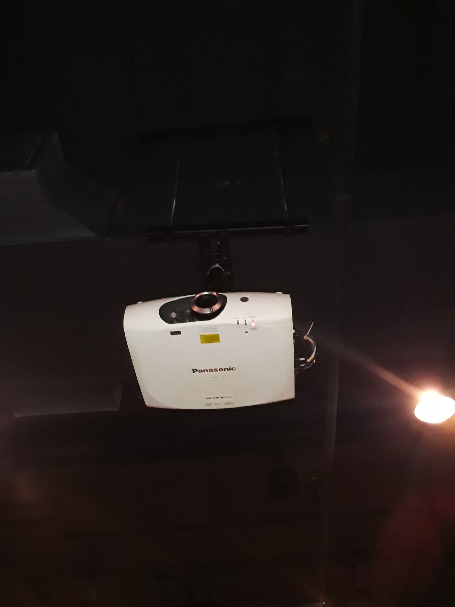 A white projector is hanging from the ceiling in a dark room