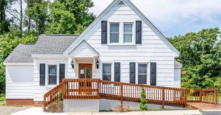 White house with brown ramp and shutters, set in front of trees.