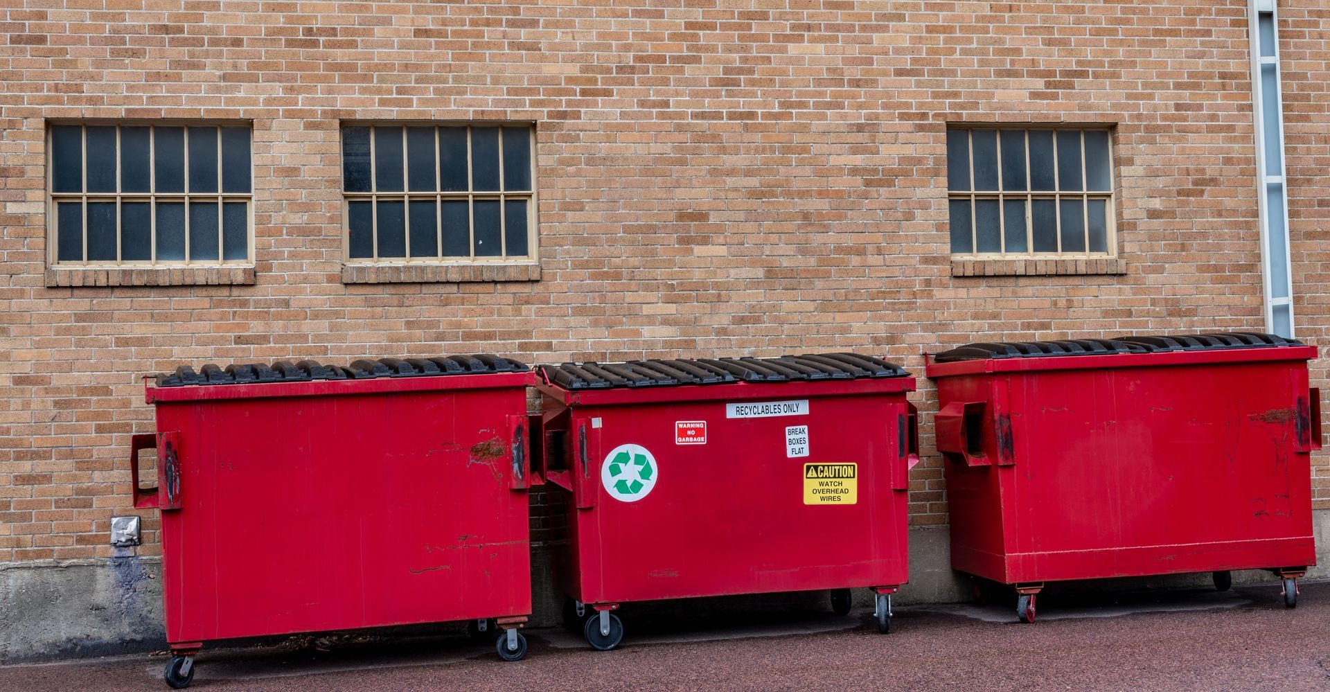 Three red dumpsters are parked in front of a brick building.