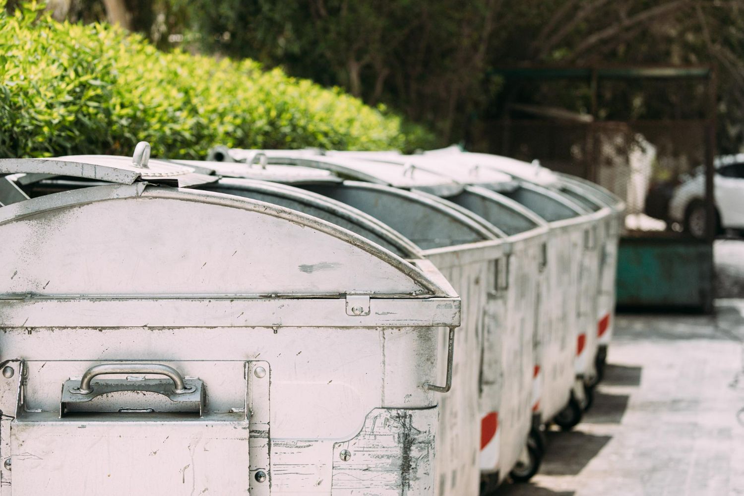 A row of white dumpsters are parked in a parking lot.