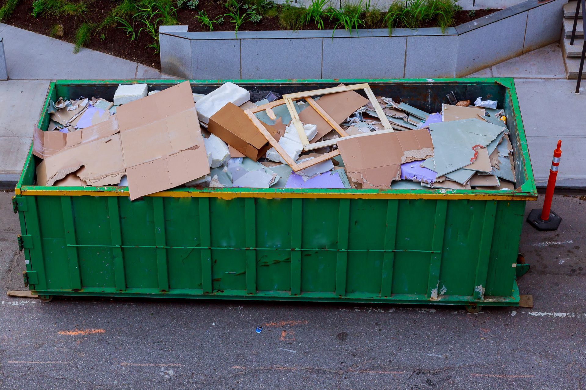 A green dumpster filled with cardboard boxes is on the side of the road.