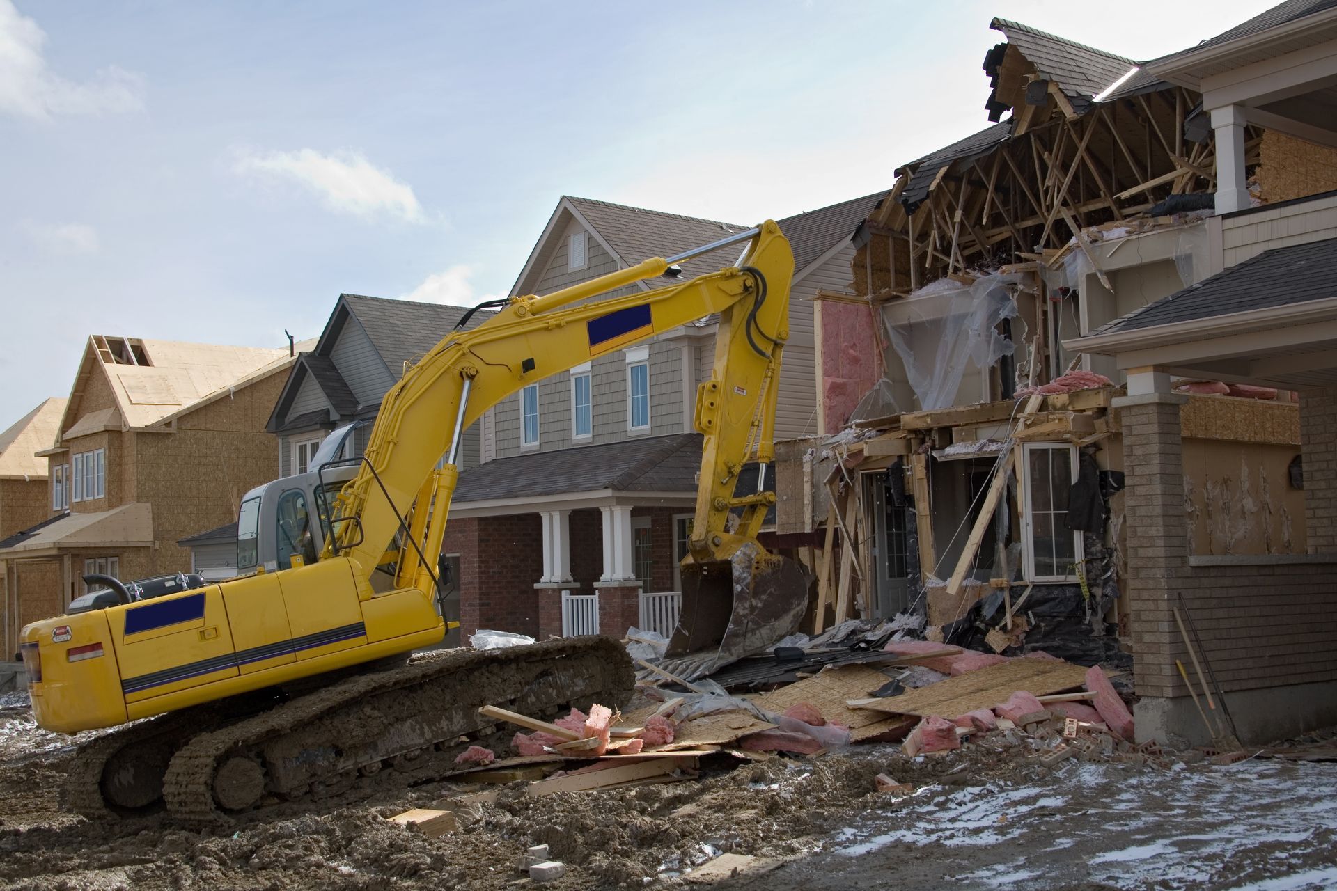 A yellow excavator is demolishing a house in a residential area.