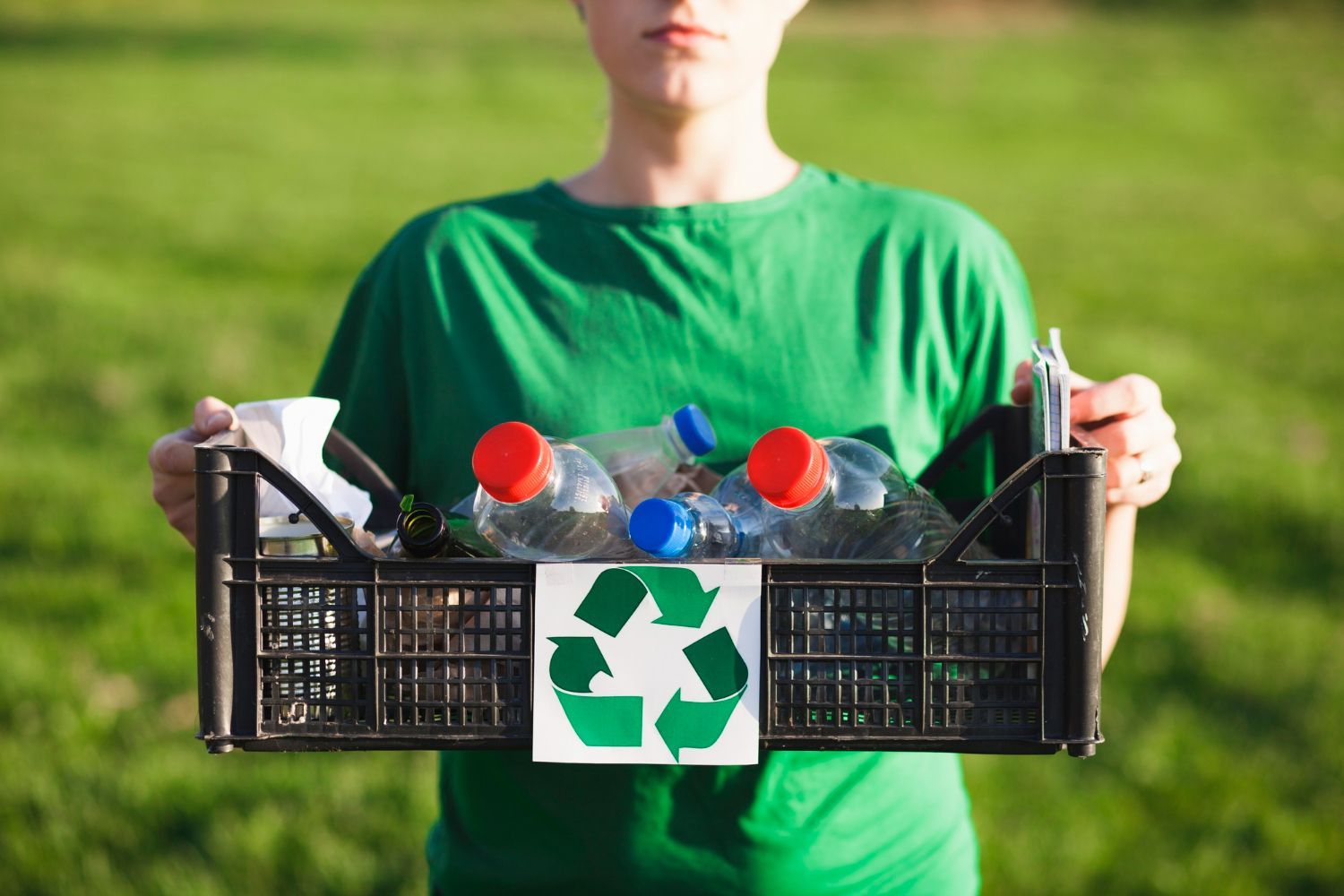 A person in a green shirt is holding a crate full of plastic bottles.