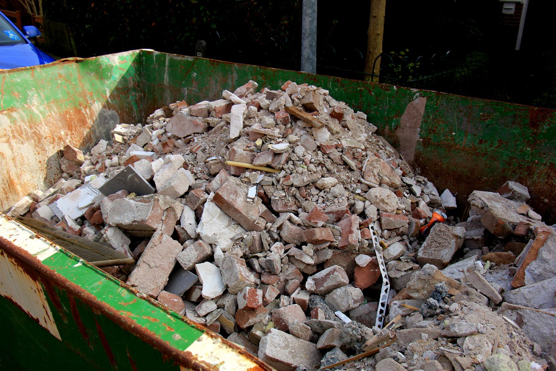 A green dumpster filled with a pile of bricks and rocks.