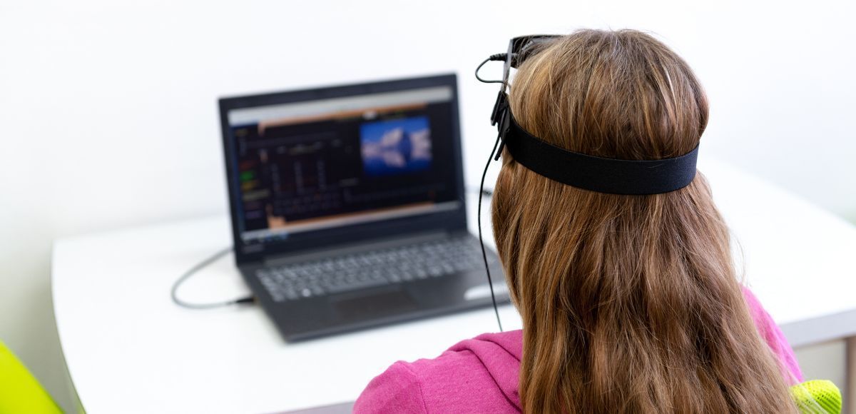 Person wearing a headset watching a laptop screen with code in a bright office.