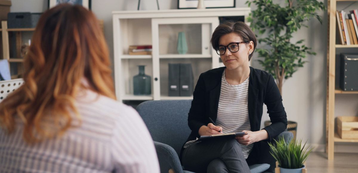 Therapist speaking with a seated client in a bright office with shelves and plants