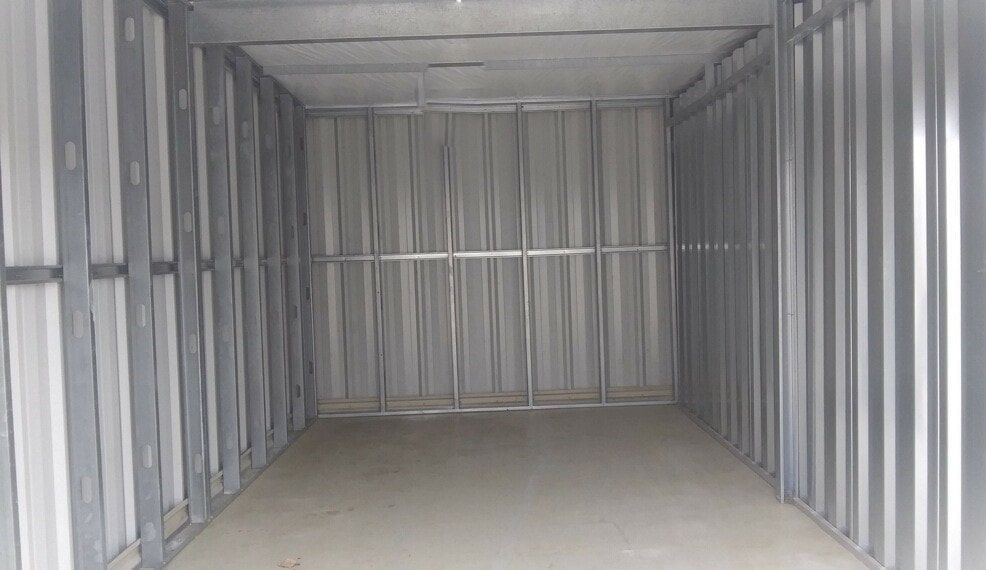 Empty metal storage unit interior. Grey walls, floor, and ceiling.