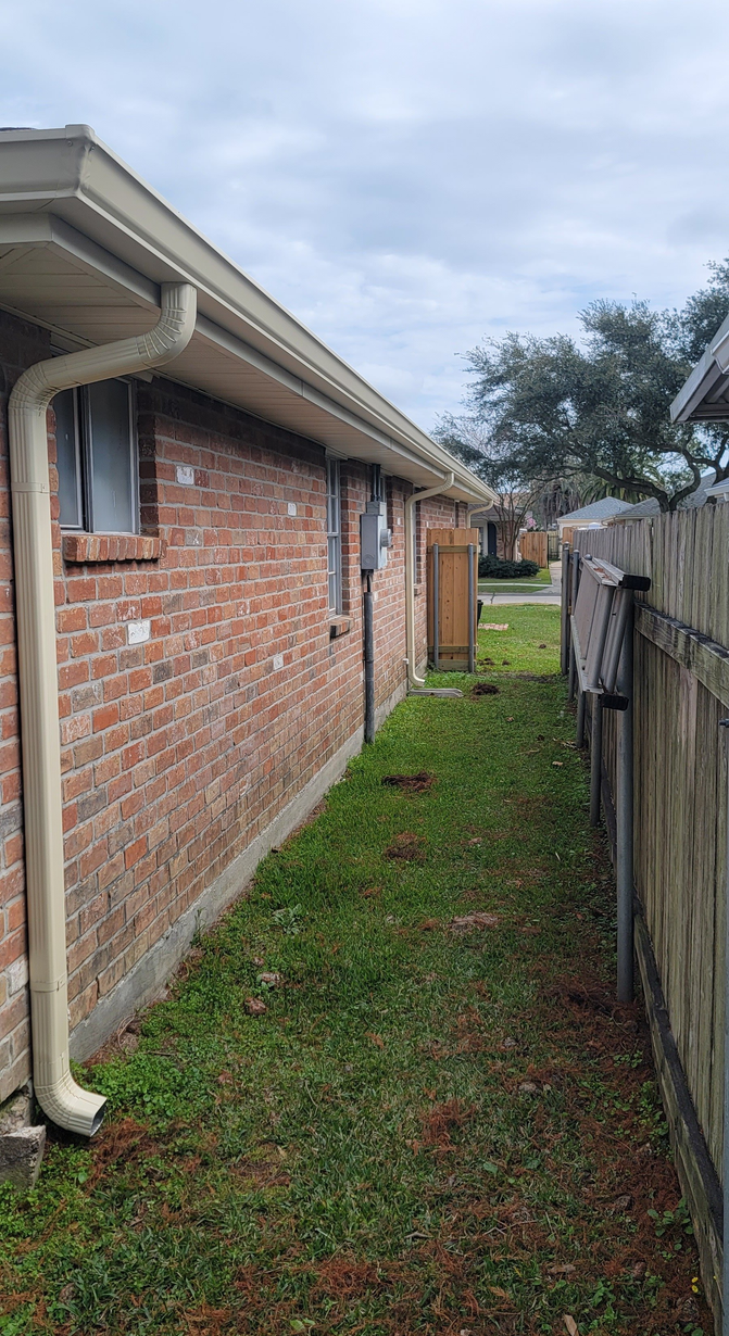 A brick house with a gutter on the side of it and a wooden fence.