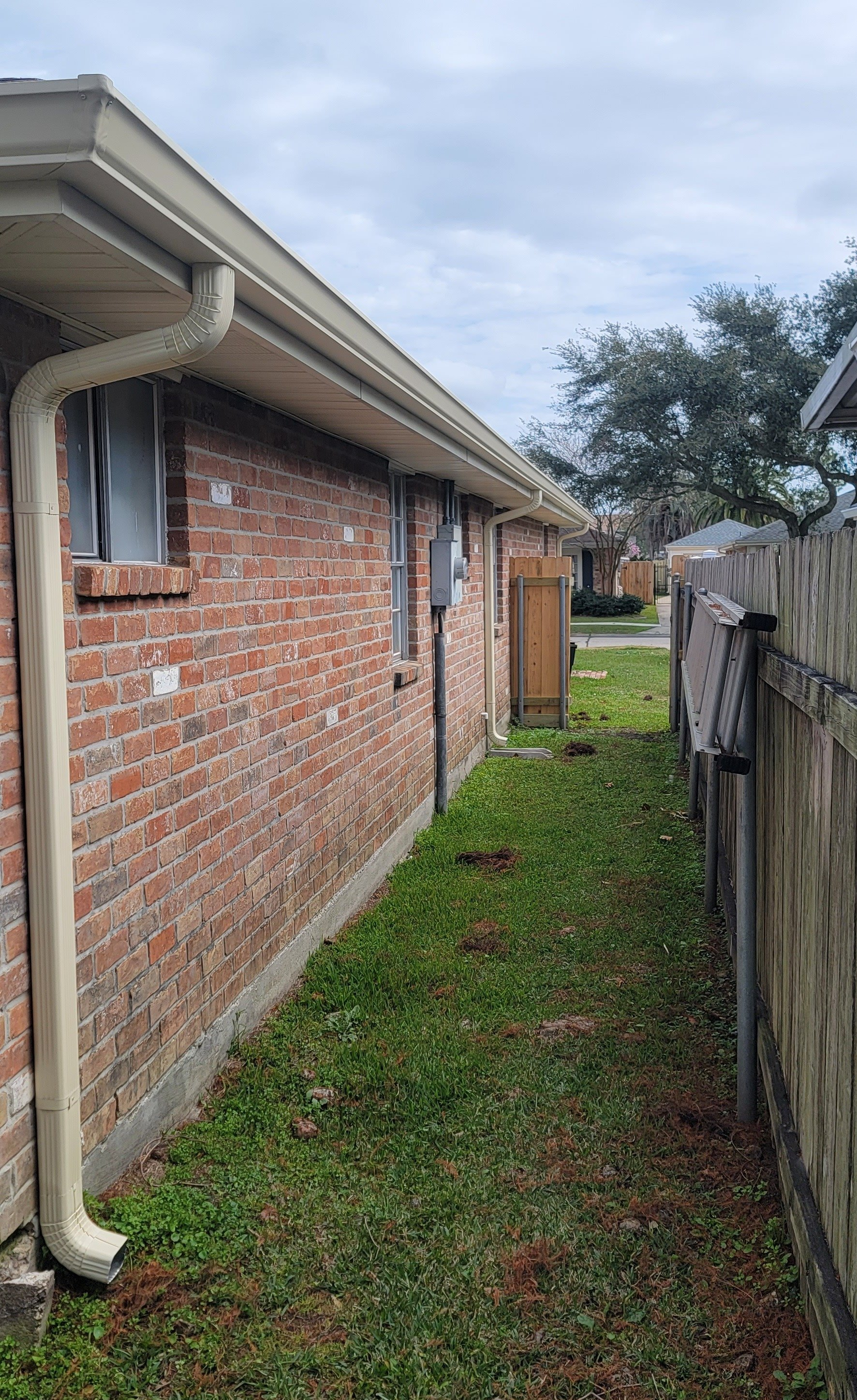 A brick house with a gutter and a wooden fence in the backyard.