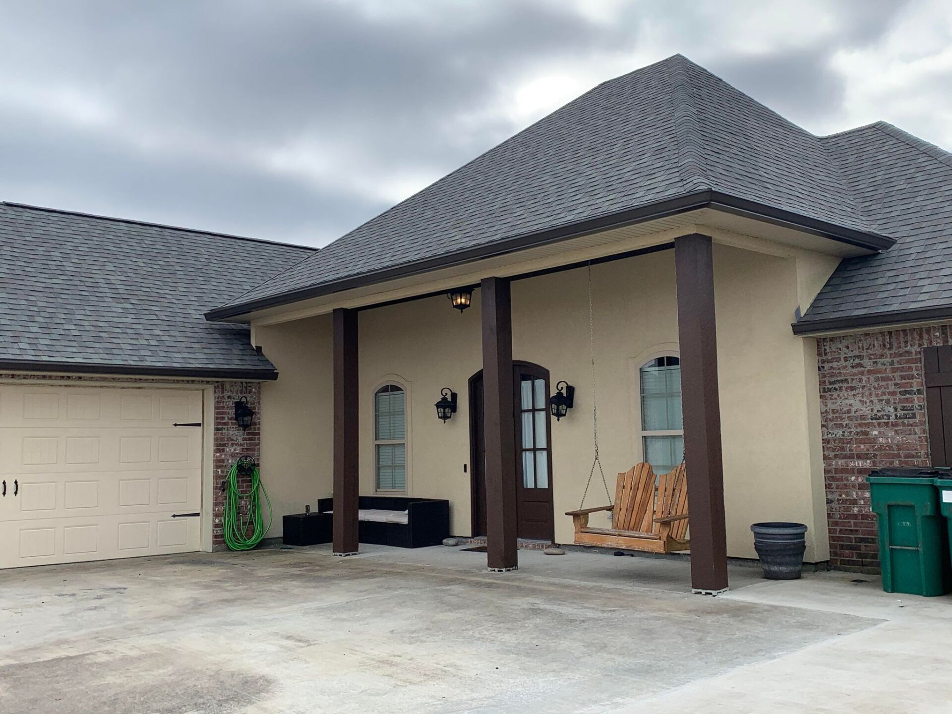 A house with a porch and a green trash can in front of it.