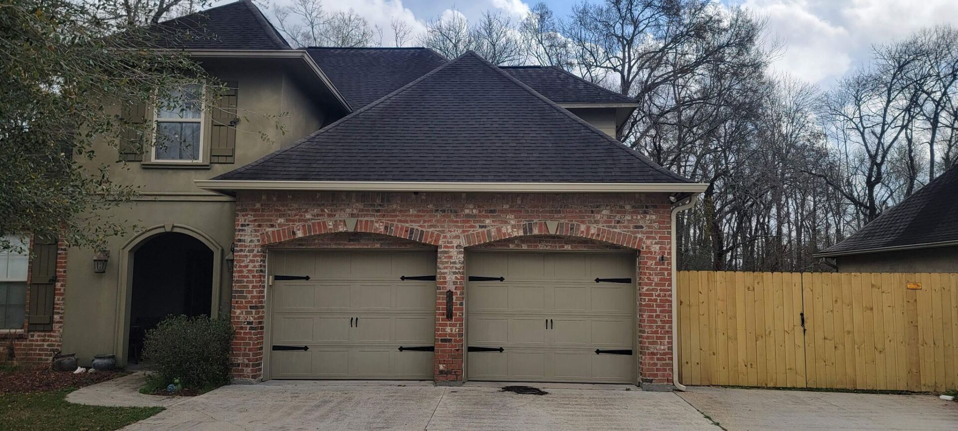 A large house with two garage doors and a wooden fence in front of it.
