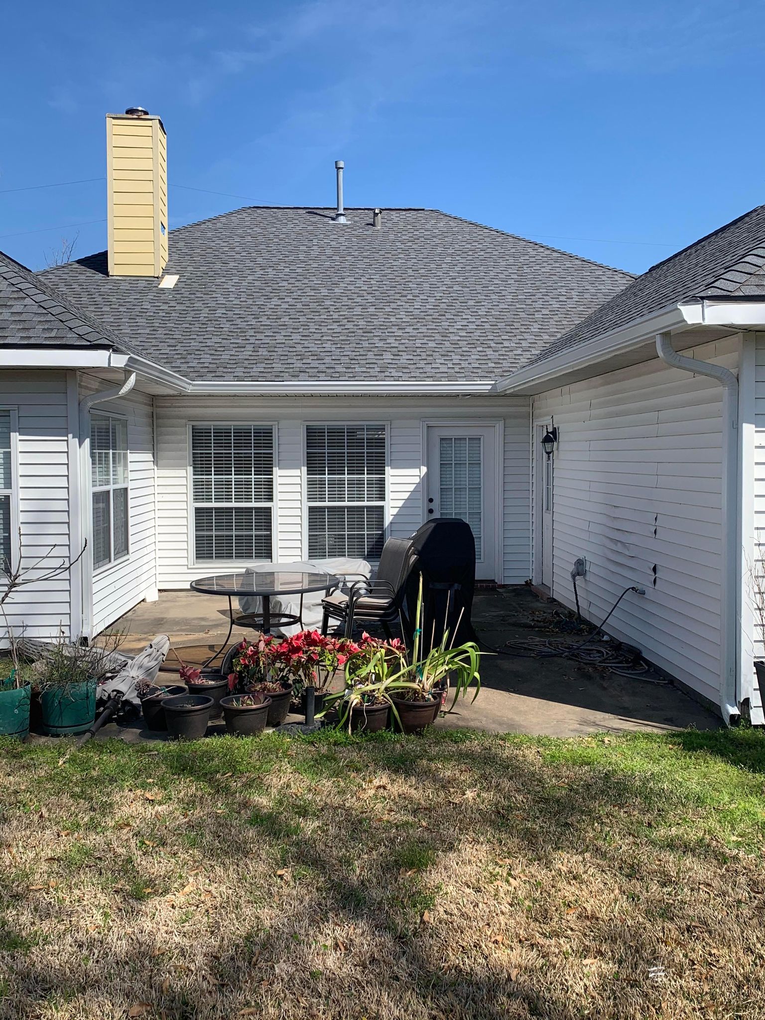 A white house with a gray roof and a patio in front of it.