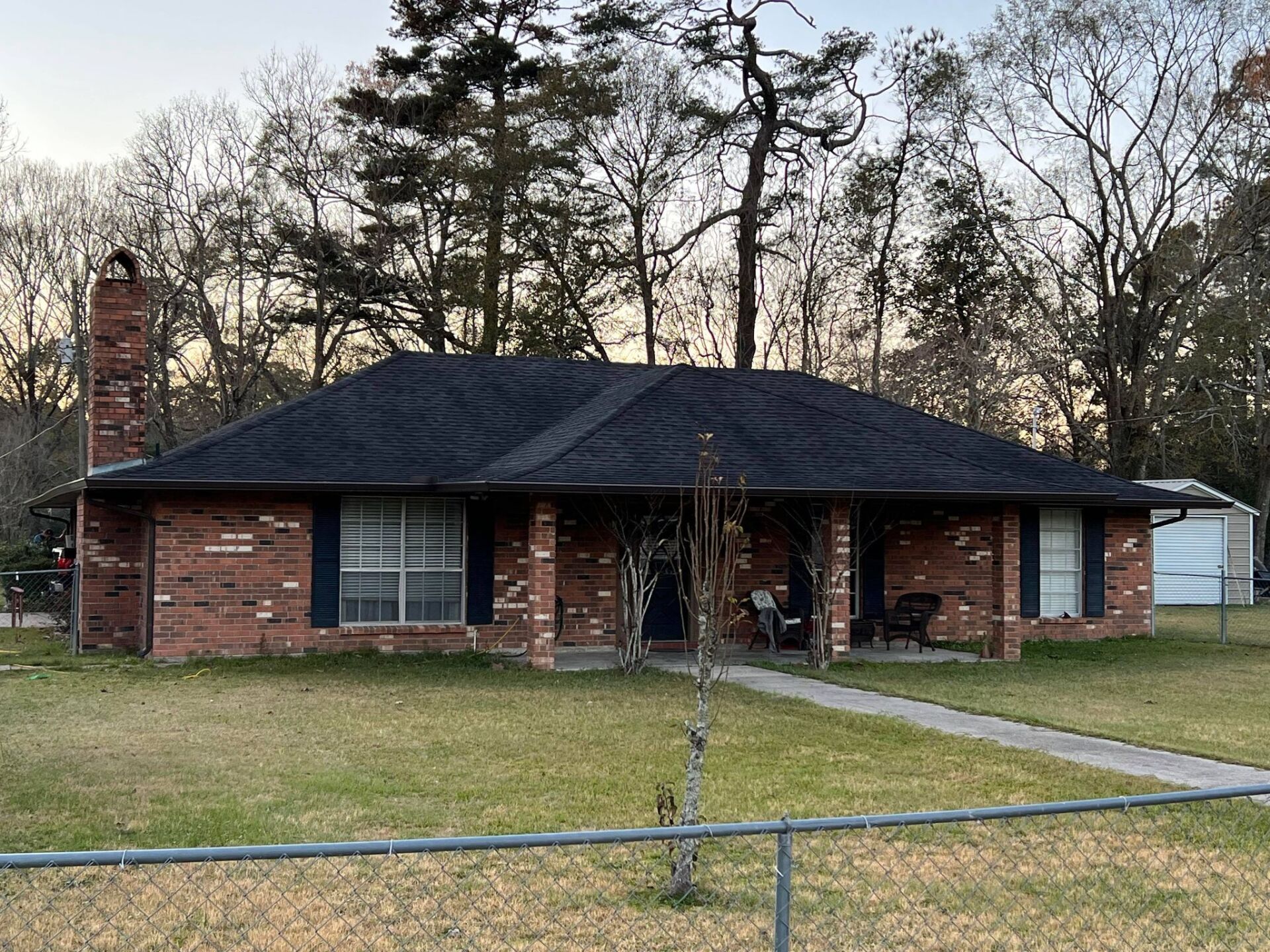 A brick house with a black roof and a fence in front of it.
