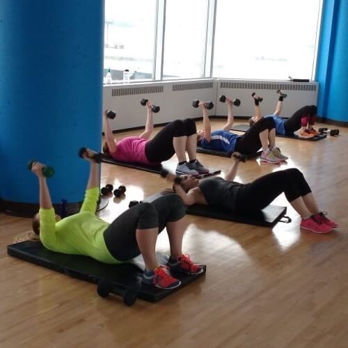 People doing dumbbell exercises on mats in a bright fitness studio