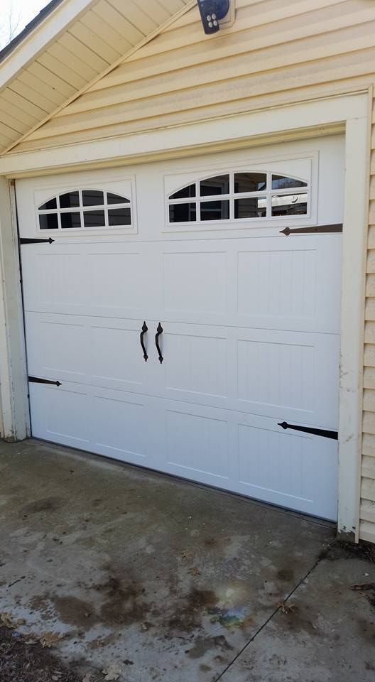 A white garage door with black handles is sitting on the side of a house.