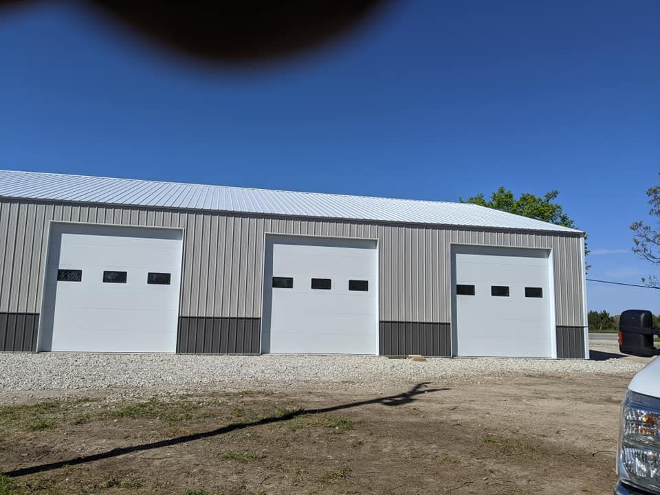 A large building with three garage doors and a truck parked in front of it.