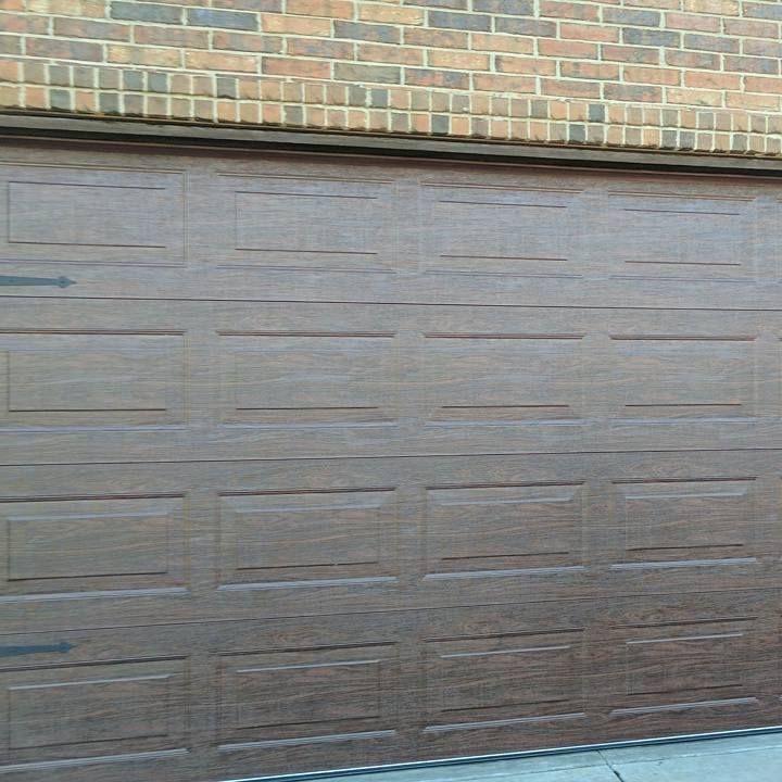 A brown garage door with a brick wall in the background