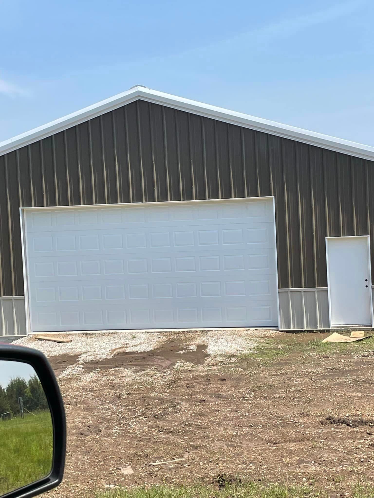 A large barn with a white garage door is sitting on top of a dirt hill.