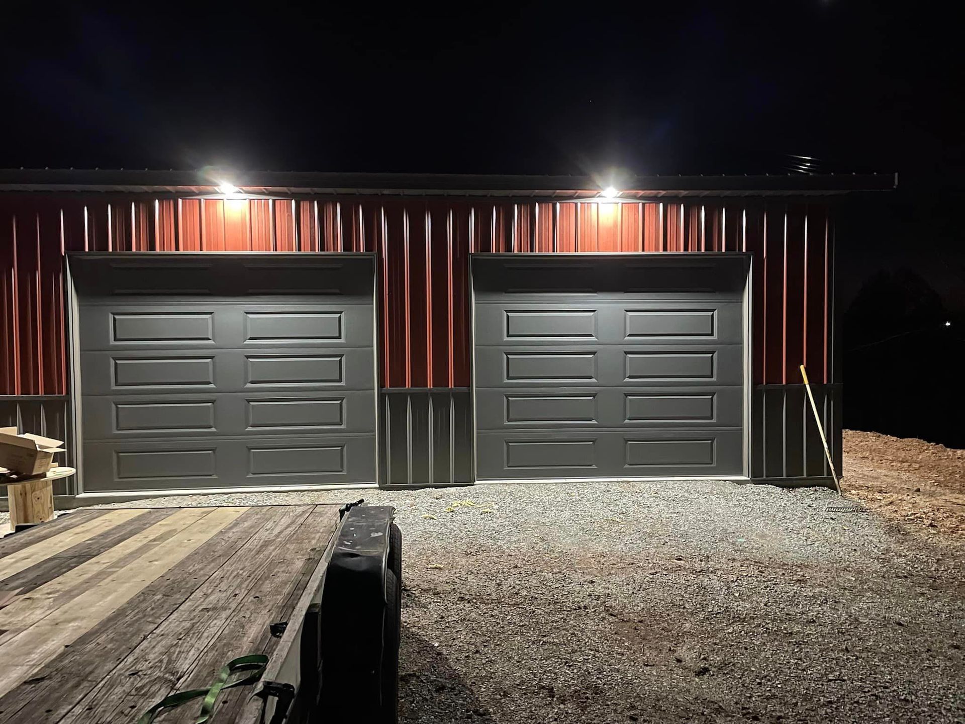 A garage with two garage doors is lit up at night.