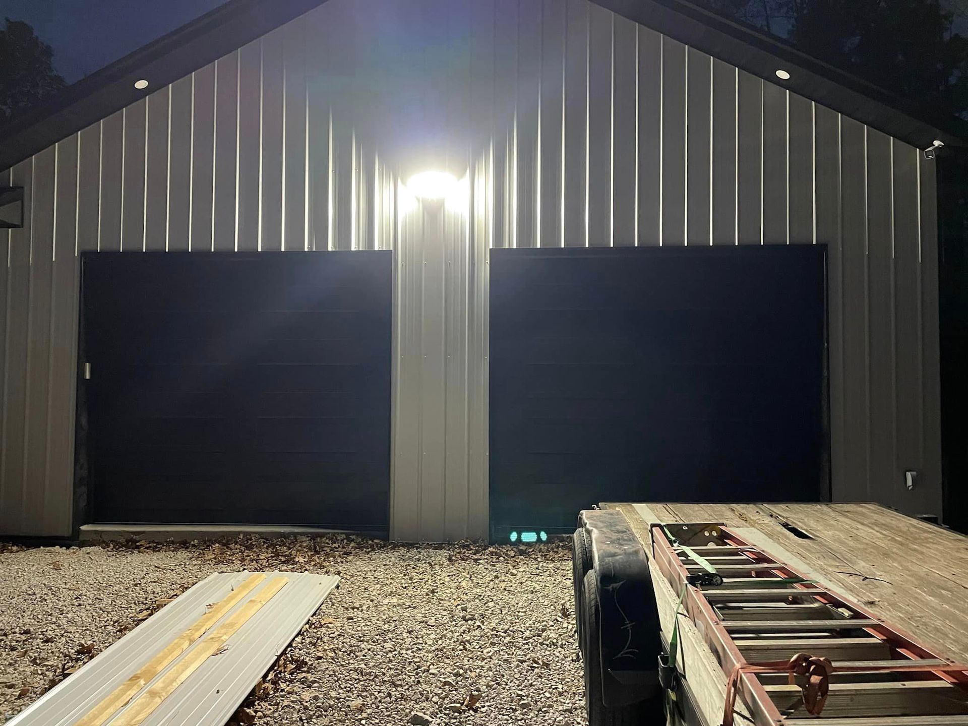 A trailer is parked in front of a garage at night.