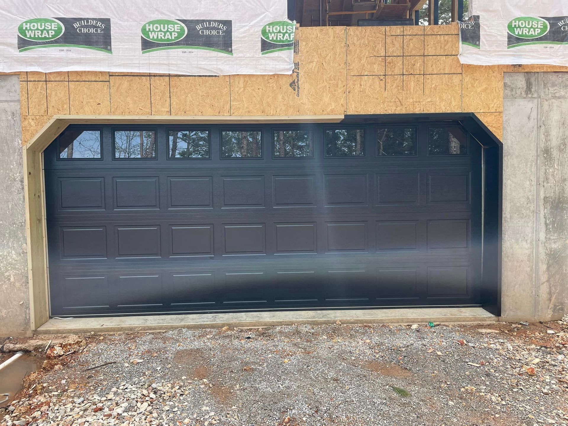 A black garage door is sitting in front of a house under construction.