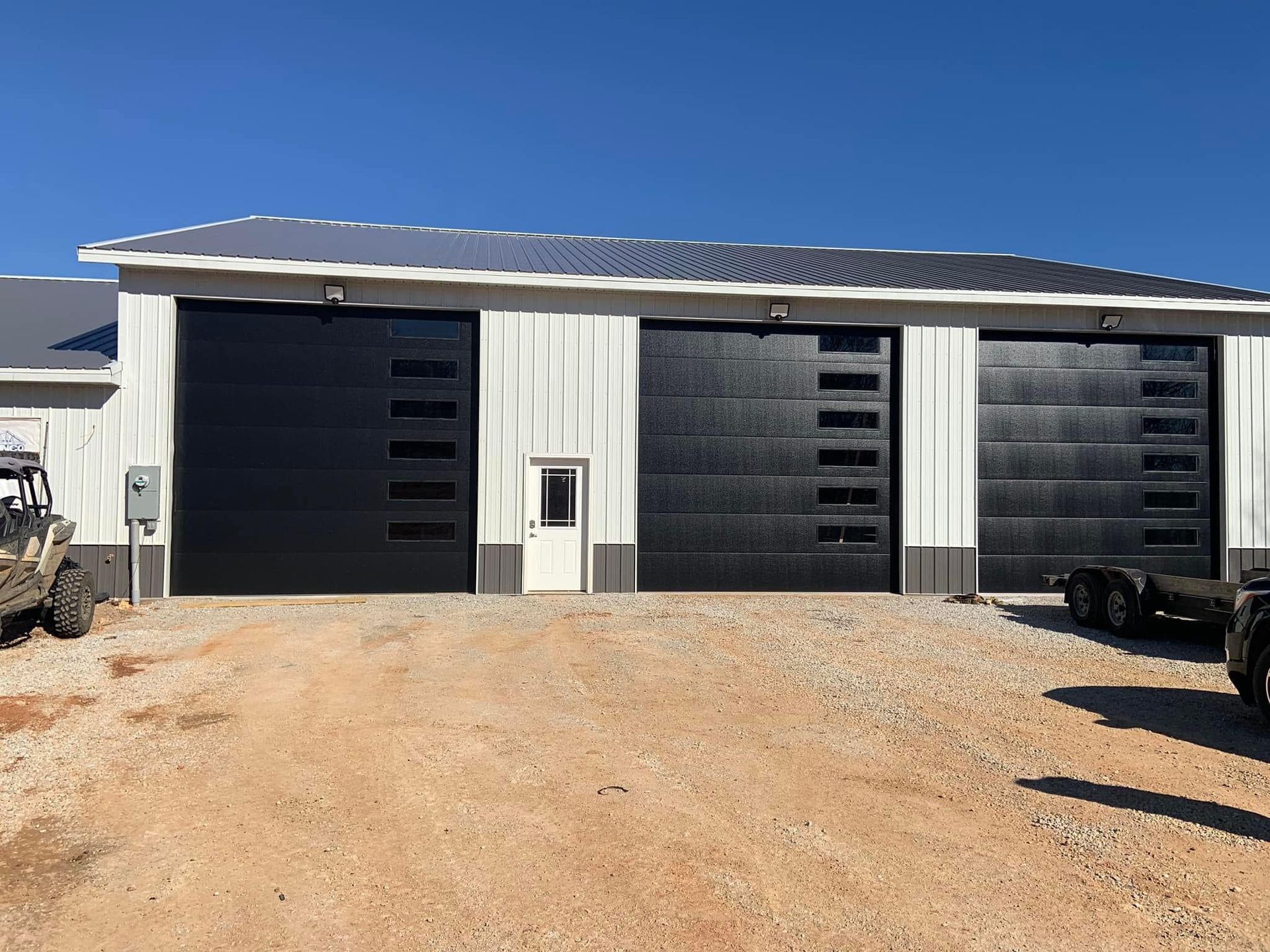 A garage with three black garage doors and a jeep parked in front of it.