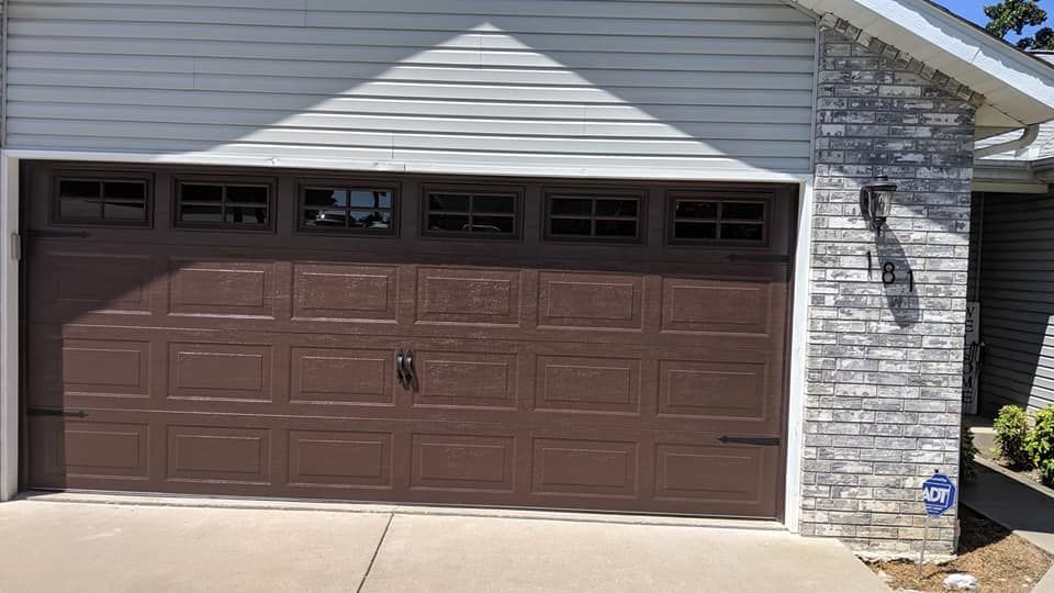 A brown garage door is sitting in front of a white brick house.