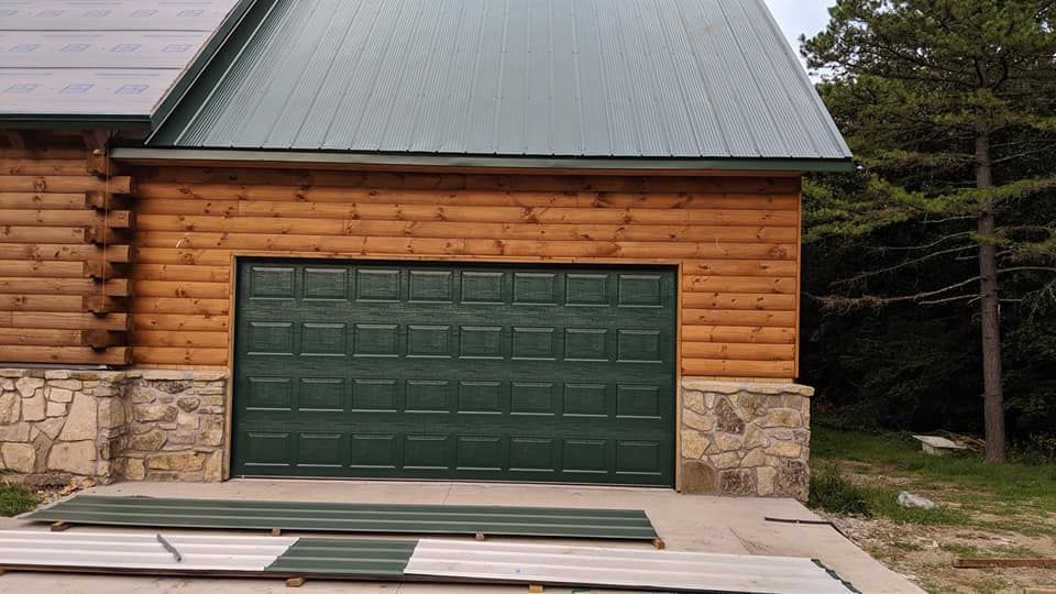 A log cabin with a green garage door and a green roof.