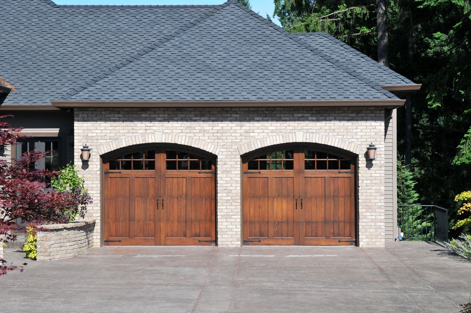 Front view of a residential home with two wooden arched garage doors, light-colored brick exterior, 