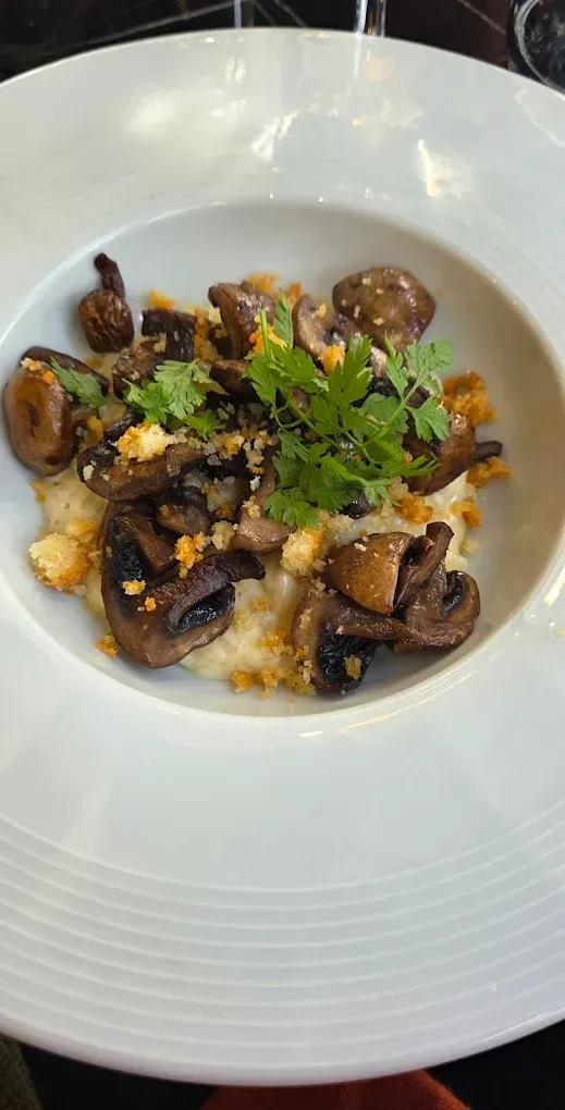 Champignons et garniture sur une polenta crémeuse dans un bol blanc.