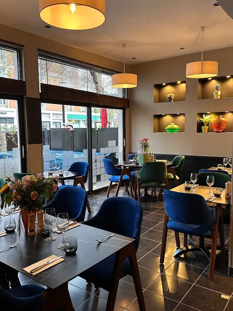 Intérieur de restaurant avec chaises en velours bleu, tables dressées et éclairage décoratif.