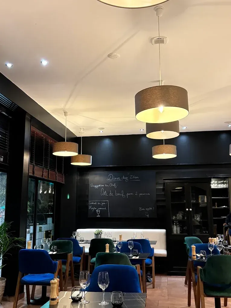 Intérieur du restaurant Chez Dhan Le Havre avec murs sombres, chaises en velours et tables dressées pour le repas.