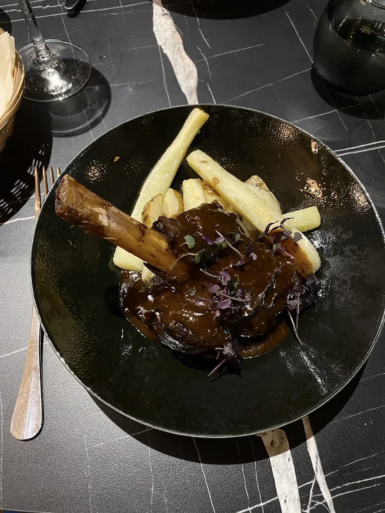 Jarret d'agneau accompagné de panais rôtis, servi sur une assiette noire.