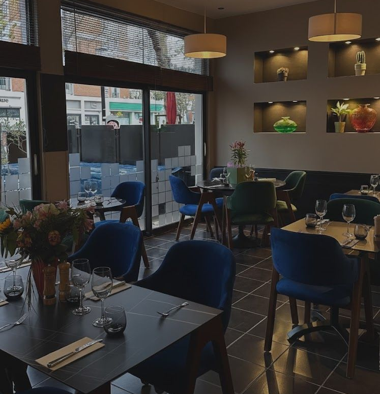 À l'intérieur d'un restaurant au sol carrelé foncé, les tables sont dressées pour le repas