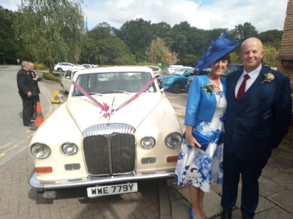 A lady and a man beside a white vintage wedding car