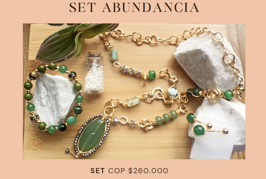 Conjunto de joyería "Abundancia". Incluye collar, pulsera y anillo con cadenas de oro y piedras verdes, expuestos sobre madera y roca.