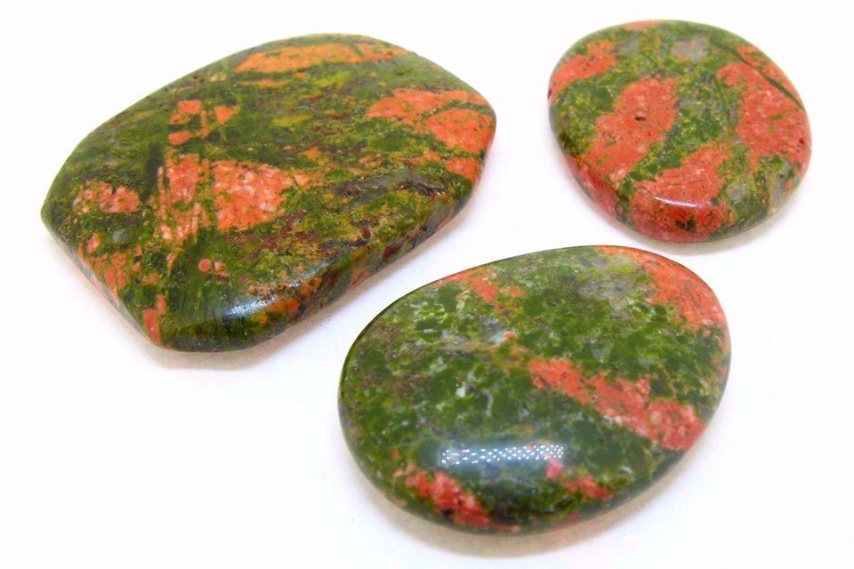 Tres piedras de Unakita lisas y pulidas; apariencia moteada en verde y naranja.