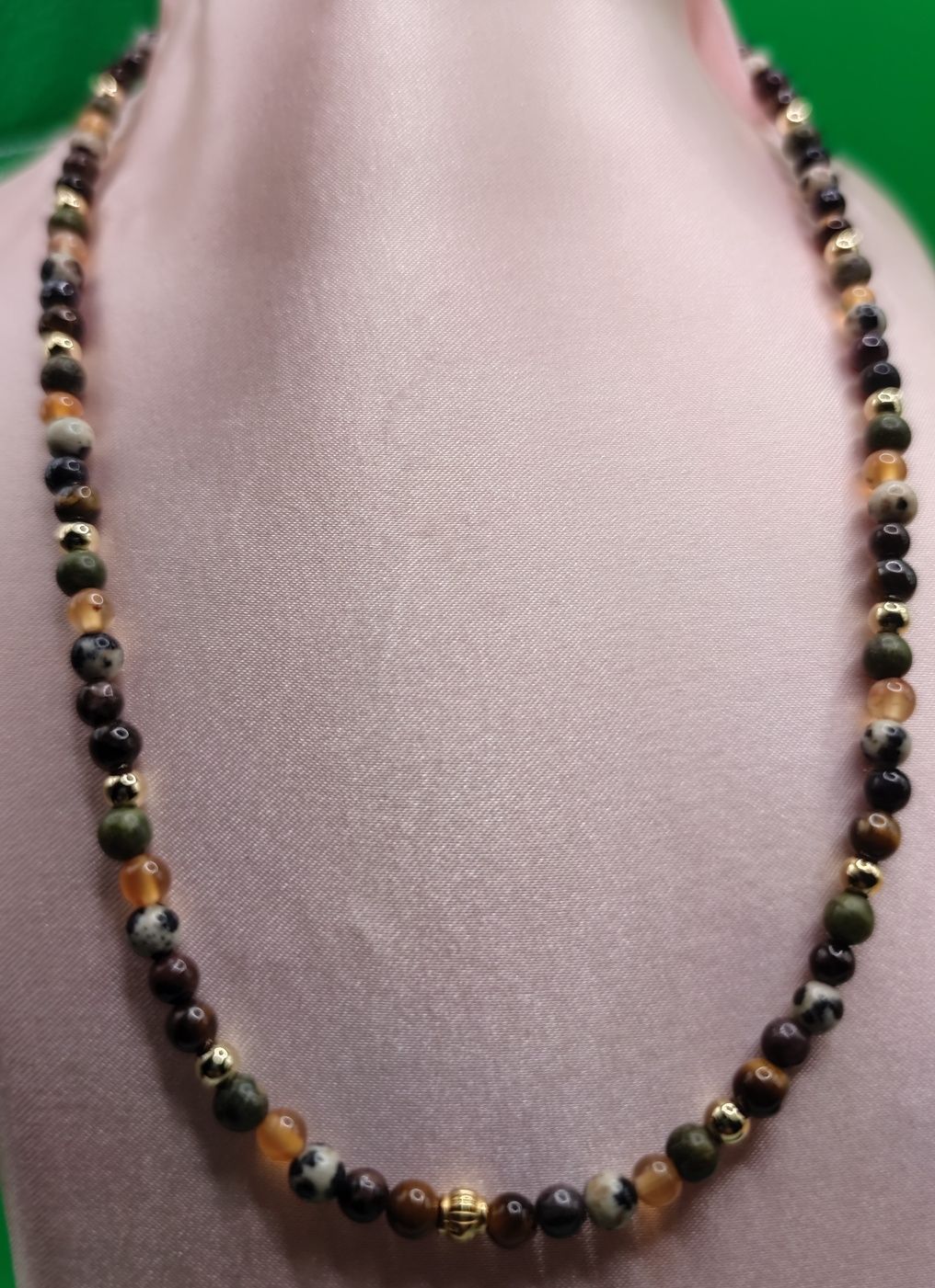 Un collar de cuentas con varias cuentas de color marrón, negro, verde y dorado, expuestas sobre un fondo rosa.