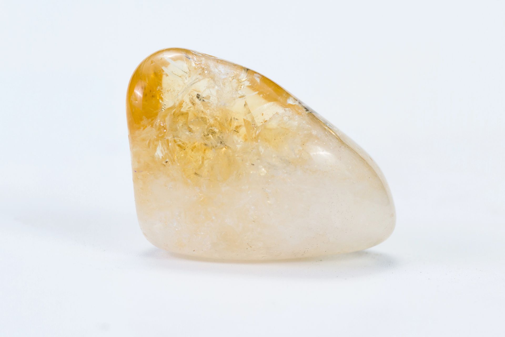 Cristal de citrino pulido, mayoritariamente translúcido con inclusiones de color amarillo anaranjado, que reposa sobre una superficie blanca.