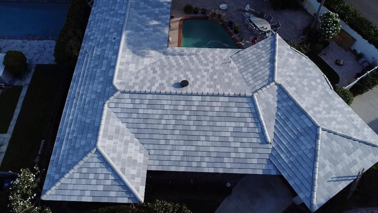 Overhead view of a house with a light gray shingle roof, a pool in the backyard, and a driveway in front.