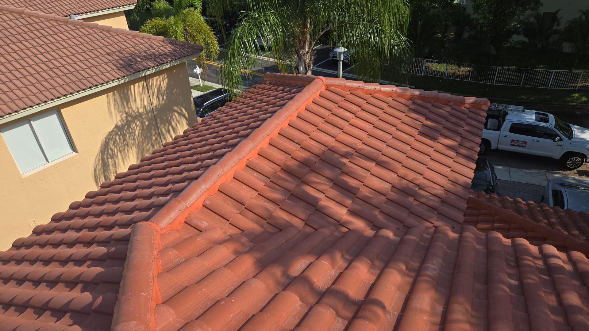 Red tile roof on a sunny day; partially visible buildings and a white truck with logo.