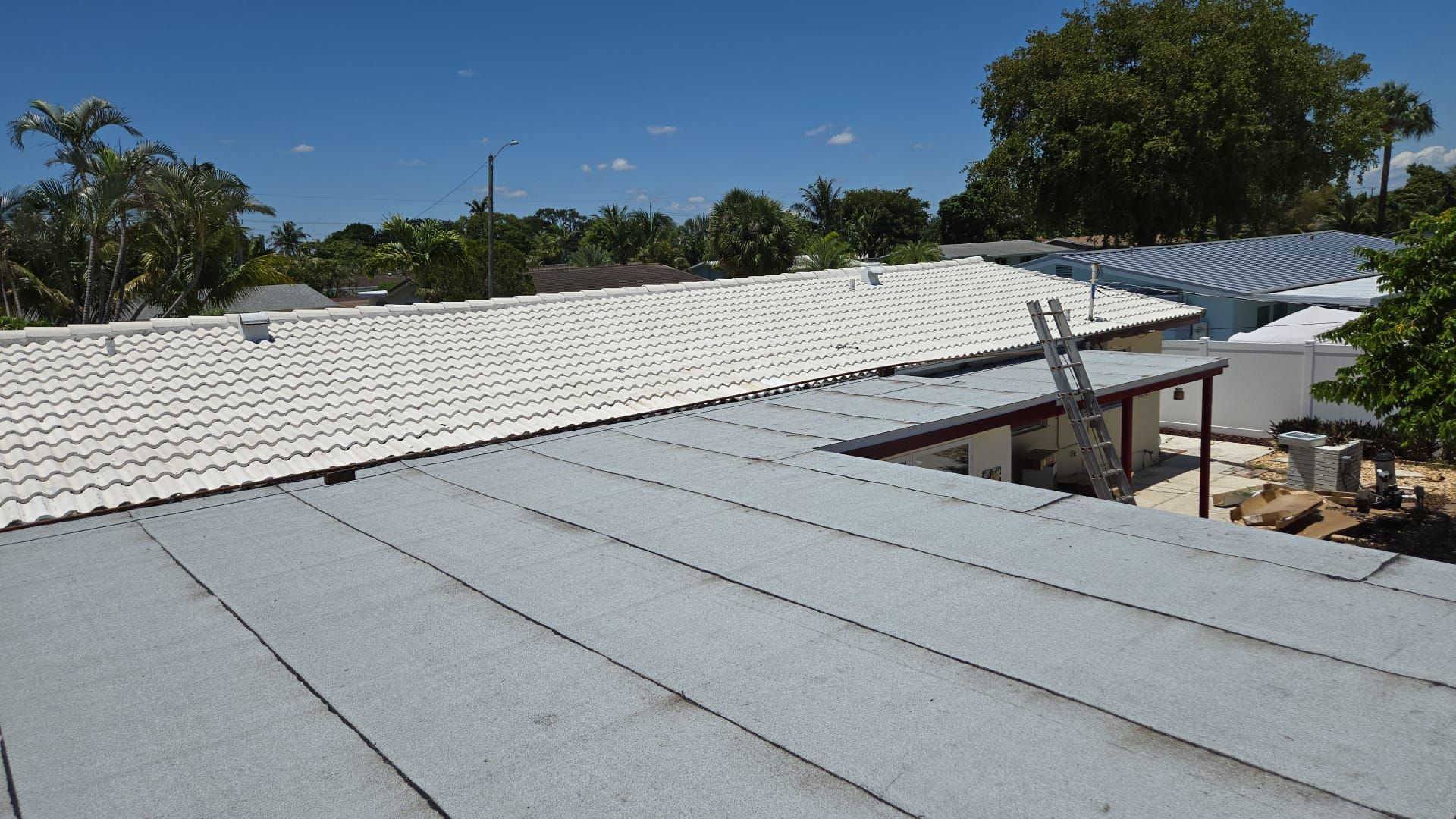 View of multiple rooftops on a sunny day. The closest roof is gray, other roofs are white and have metal railings.