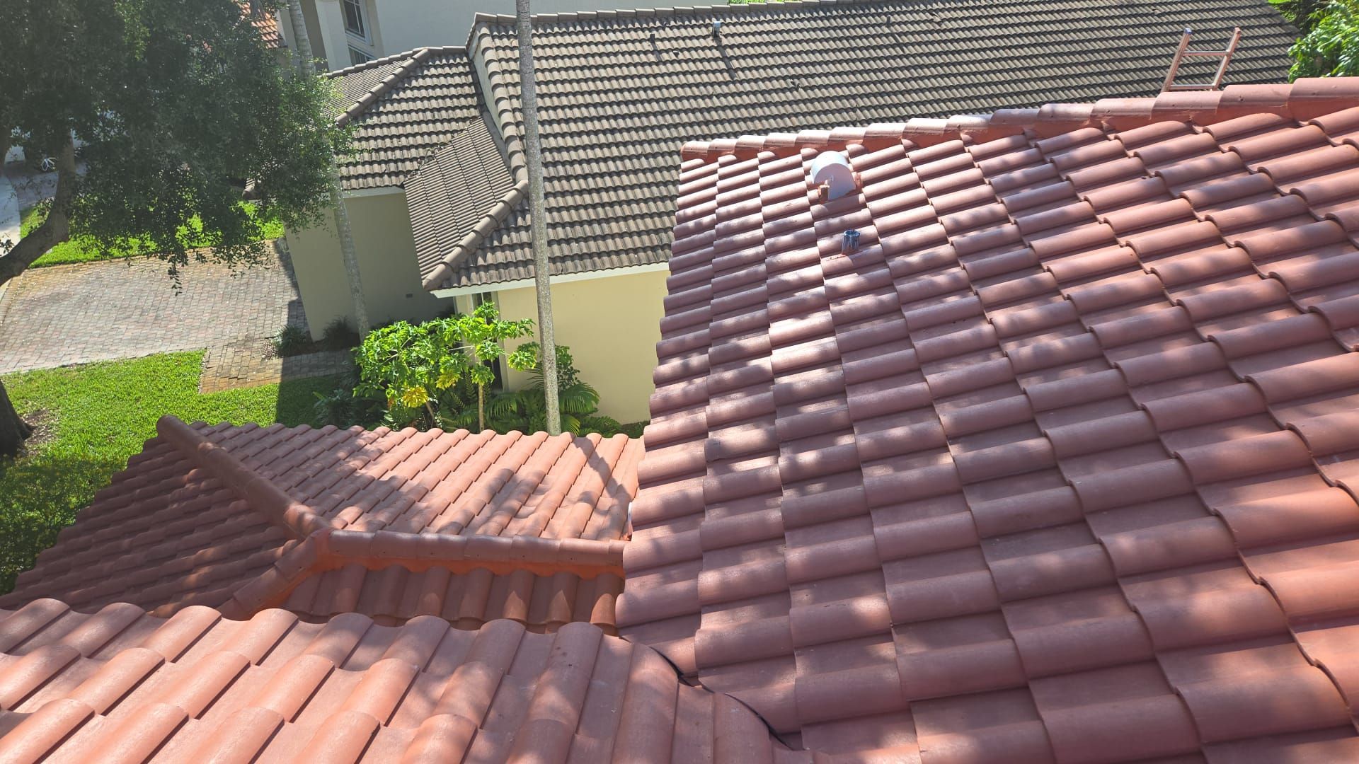 Red tile roofs of two houses, seen from above on a sunny day. One roof has a white vent.